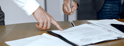 Mão apontando a um documento indicando local de assinatura
