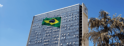 Foto Do Edifico Sede de Brasilia, com a bandeira do Brasil á frente.