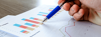 Mão segurando caneta em cima de uma folha com gráficos estatísticos.