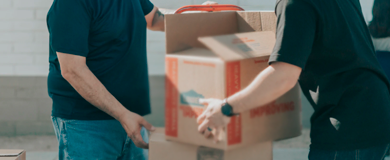 Duas pessoas carregando caixas de papelão. Ambas com camisa azul escuro e calça jeans