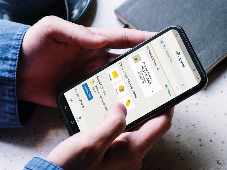 App mãos segurando celular exibindo a tela de atendimento do aplicativo dos correios