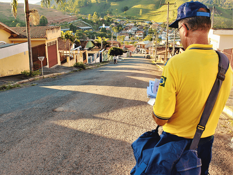 Carteiro vendo correspondências que precisam ser entregues ao longo de uma rua.