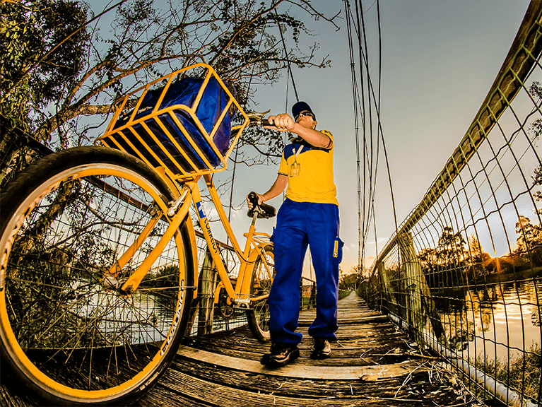 Carteiro com bicicleta dos Correios passando por uma ponte localizada acima de um rio