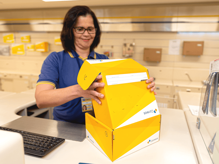 Atendente dos Correios, embalando encomenda em caixa própria da ECT. Benefícios