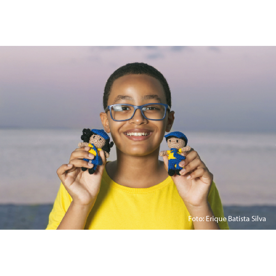 Criança de óculos segurando em suas mãos dois bonecos de miniaturas dos carteiros dos Correios