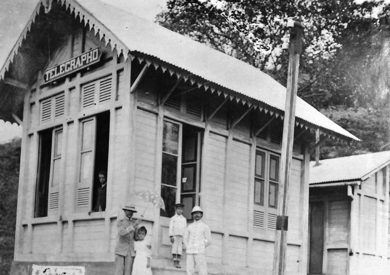 Imagem em preto e branco de uma casa de esquina com quatro janelas e uma placa com o nome "telegrapho". Em sua frente dois homens e duas crianças.