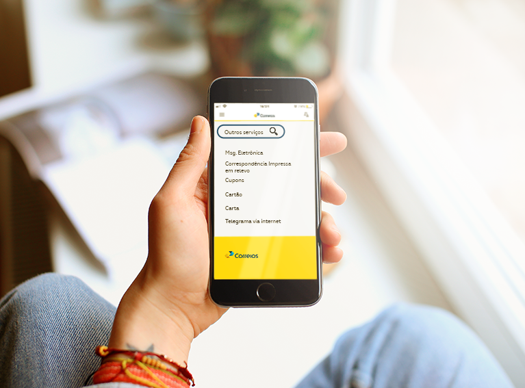 Mão segurando celular. Em sua tela o aplicativo dos Correios.