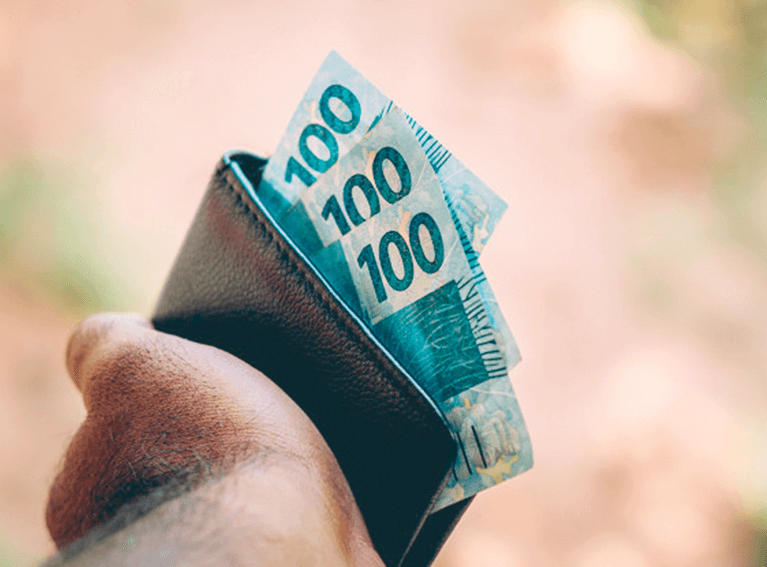 Vale Postal Mão segurando uma carteira com três notas de cem reais expostas