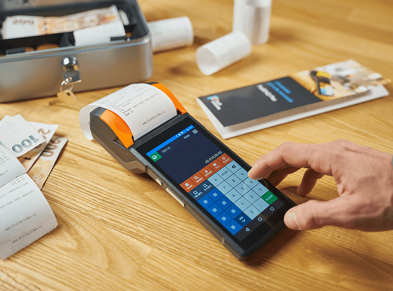 Vale Postal Empresas Sob a mesa uma caixa aberta com notas de dinheiro, papéis e uma máquina de cartão de crédito com uma mão digitando um número.