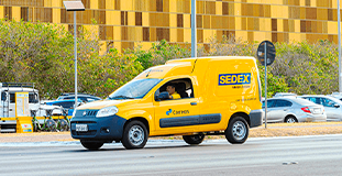 Foto de um carro amarelo dos Correios transitando por uma rua.