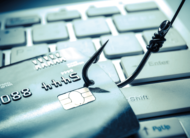 Cartão de crédito sendo fisgado por um anzol, ao fundo um teclado de computador