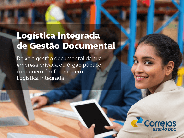 Foto de mulher morena e terno bege olhando pra trás com tablet na mão em uma mesa com um homem branco de terno azul manuseando um computador e prateleiras de um armazém atrás. Frase: Logística Integrada de Gestão Documental. Deixe a gestão documental da sua empresa privada ou órgão público com quem é referência em Logística Integrada.