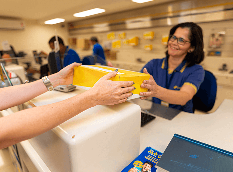 Clique e Retire dos Correios Atendente na agência dos correios recebendo encomenda para postagem